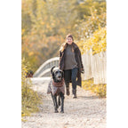 Dog wearing a brown Trixie Minot Sherpa coat while walking with its owner outdoors